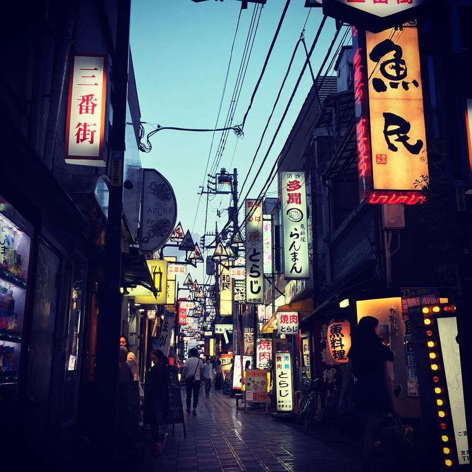 Pedestrians in a neon-lit Tokyo alley at dusk