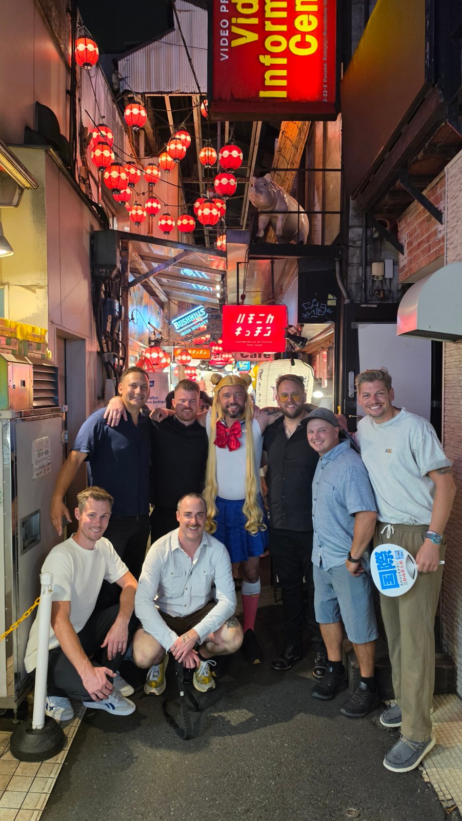 A group posing beneath red lanterns and the Harmonica Kitchen sign in a narrow alley in Kichijoji