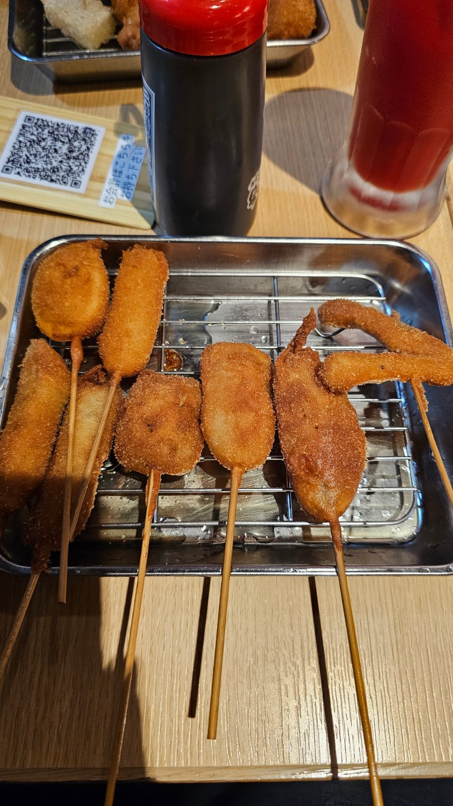Golden breaded and fried skewers arranged on a metal tray beside sauce bottles