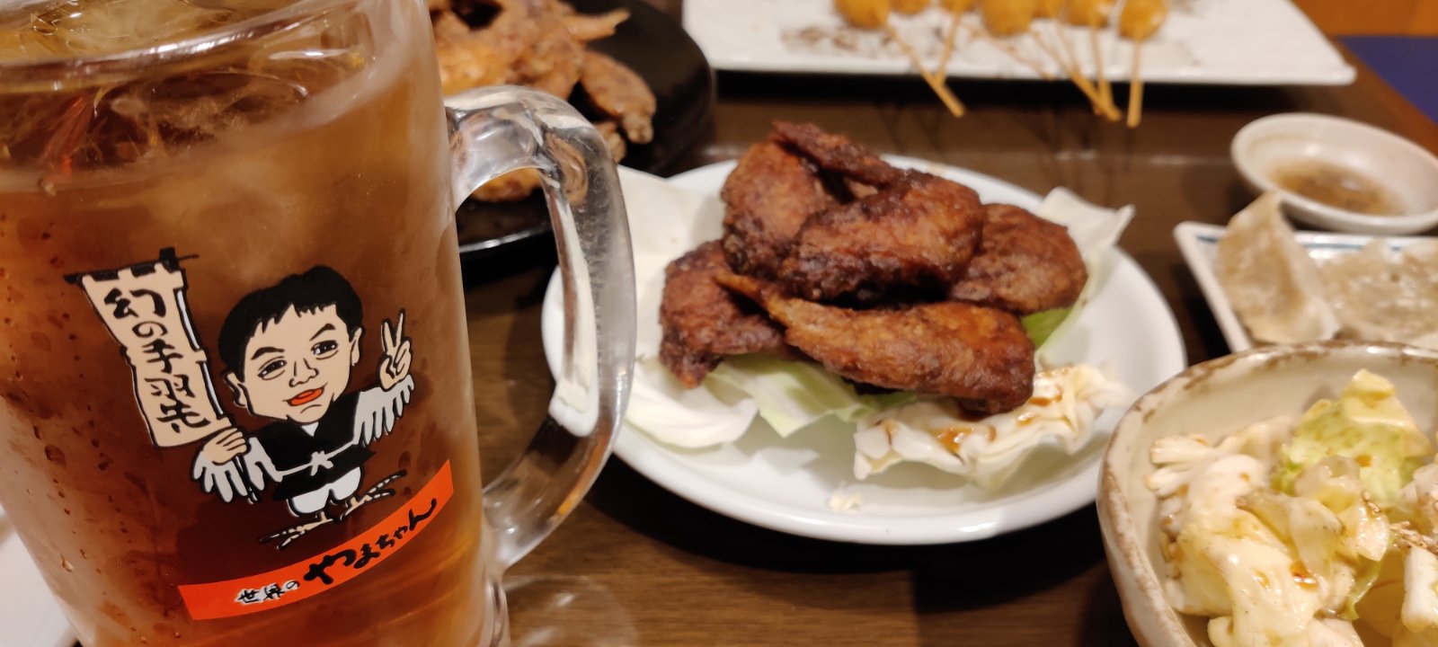 A plate of fried chicken wings and shared dishes beside a large iced drink in a Yamachan mug