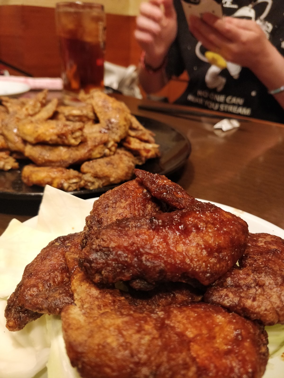 Close-up of glazed chicken wings, with another plate of seasoned wings on the table behind them