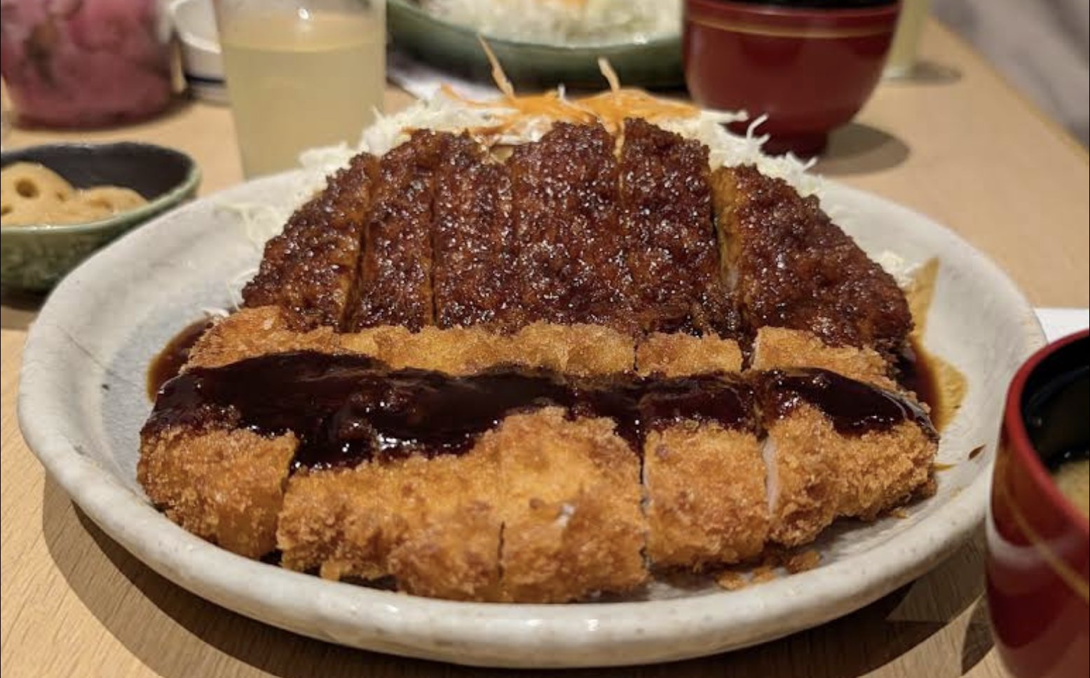 Sliced breaded pork cutlets topped with dark miso sauce, served with shredded cabbage on a large plate