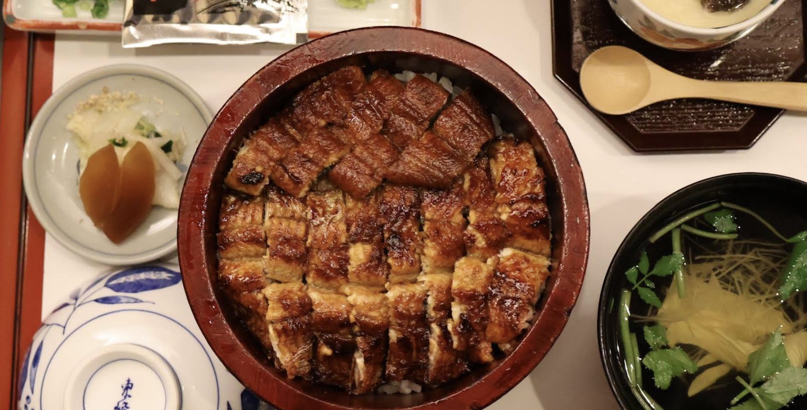 Grilled eel over rice in a wooden bowl, with soup and side dishes