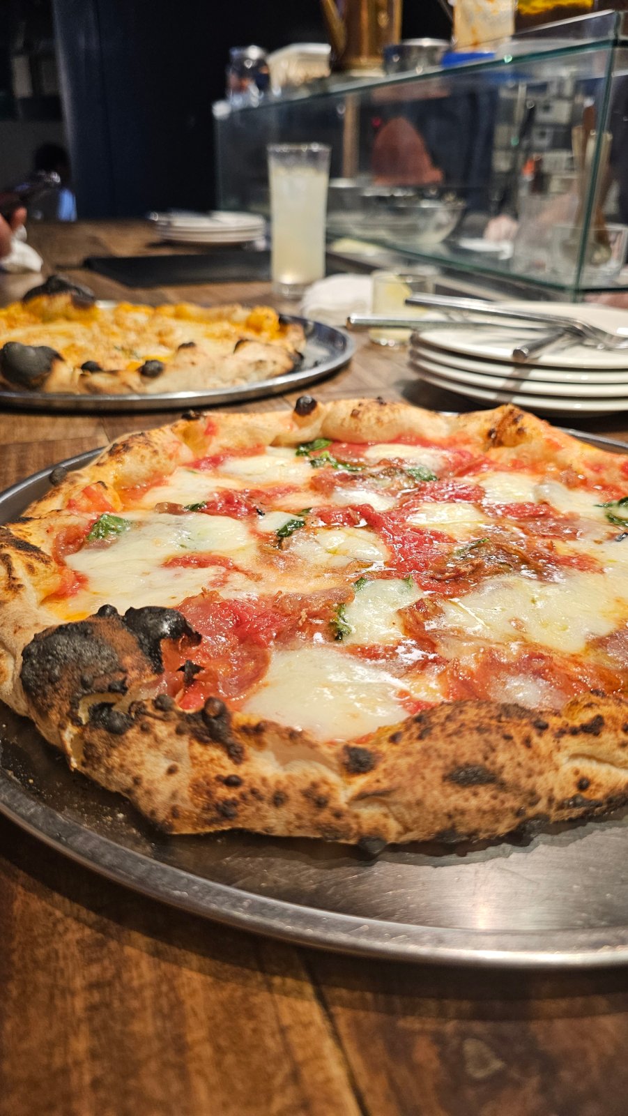 Pizza with tomato, melted cheese and basil, with another pizza on the table behind it